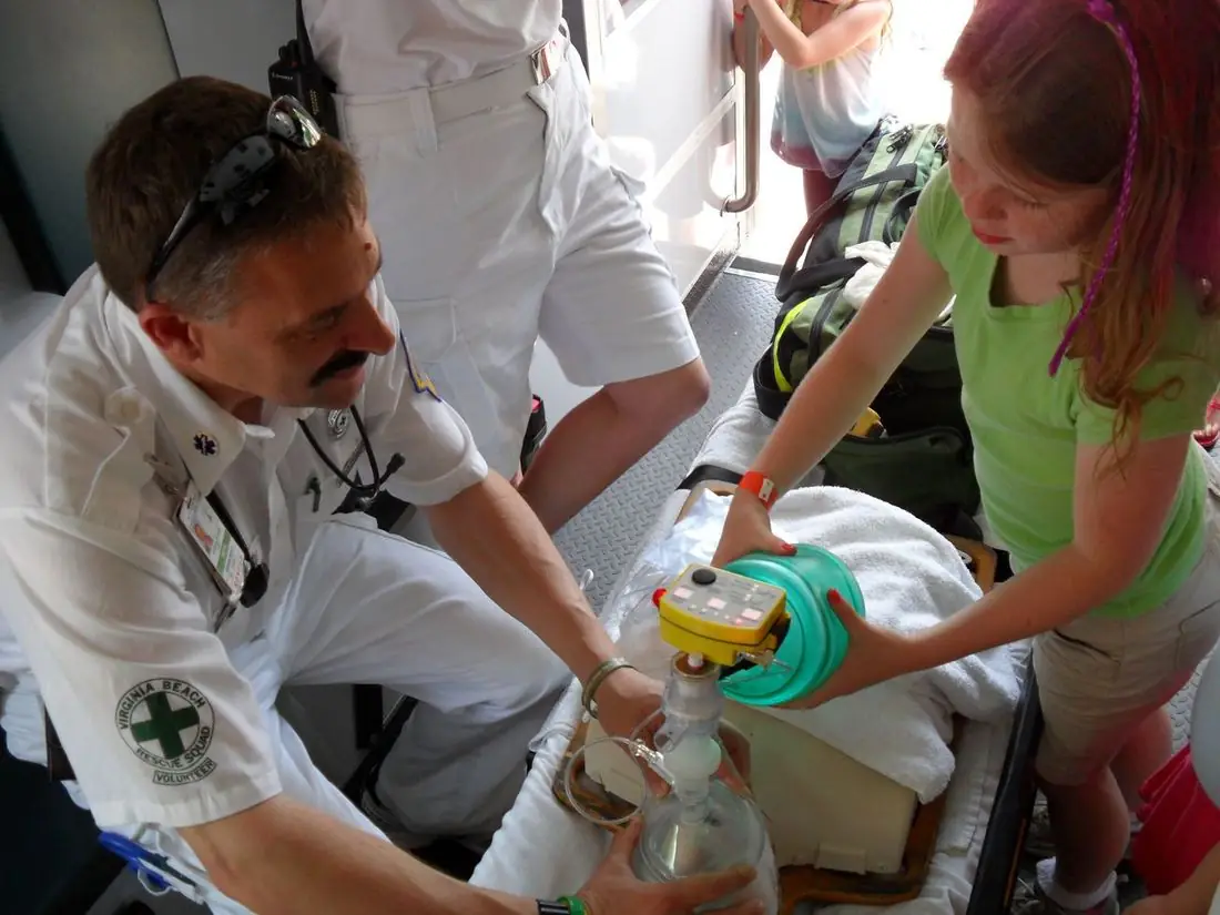 A VBVRS volunteer shows a young girl how a breathing device works in the back of an ambulance
